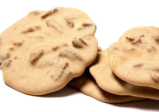 Round, flat dollops of pecan-studded, golden-brown pralines are stacked together. 