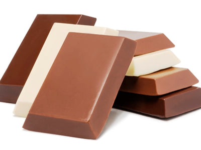 Small rectangular bars of milk, white and dark chocolate are stacked up together.