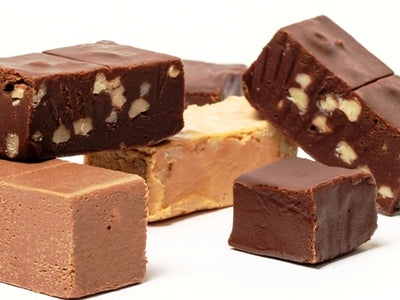 Bars of chocolate, chocolate walnut, peanut butter and maple walnut fudge are stacked together. 