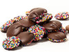 Dollops of round chocolate pieces are stacked together. Each piece has one side coated in tiny rainbow colored nonpareil candies.