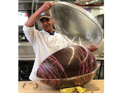 A giant chocolate molded egg is being removed from the mold.