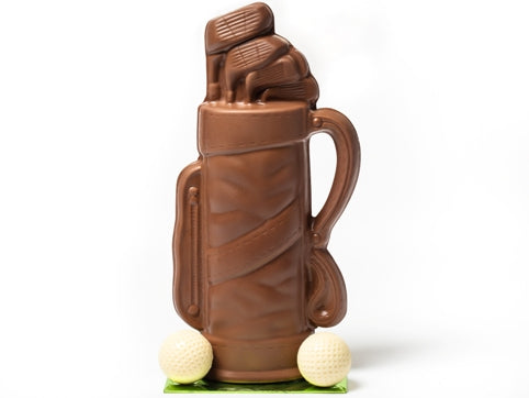 A molded chocolate Golf Bag  has clubs coming out of the top and two white chocolate golf balls sitting next to the bag.