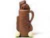 A molded chocolate Golf Bag  has clubs coming out of the top and two white chocolate golf balls sitting next to the bag.