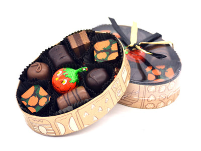 An oval box has 8 pieces of assorted chocolates plus a foil wrapped pumpkin shaped chocolate in the center. It has a clear lid and is tied with halloween raffia.