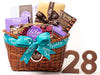 A low, oval wicker basket is tied with an aqua happy birthday ribbon. The basket holds one home assortment chocolate box, butter crunch in a purple window box, one boxed chocolate bar, a clear acrylic box filled with chocolate nonpareils, a happy birthday bar in a gold box with a brown ribbon, two chocolate numbers.