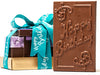 A Happy Birthday bar in a gold box is stacked with a French Assortment gift box and a window box of caramels all tied together with an aqua "Happy Birthday" printed ribbon.