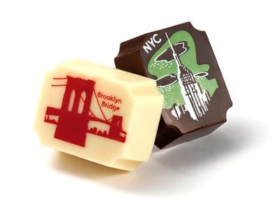 Two solid chocolate rectangular pieces, one dark chocolate and one white chocolate. They have buttercream art transfers on the top with images of the brooklyn bridge and empire state building.