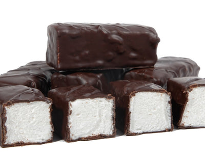 Thick bars of marshmallow enrobed in dark chocolate are lined up together. The bars are cut so that you can see the soft white marshmallow inside.