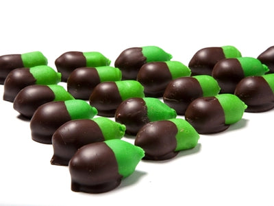 Bright green marzipan that is molded into bite-sized acorn shapes are lined up together. The acorn “cap” end is made by dipping the marzipan into 72% dark dairy-free chocolate.