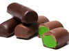 Cylinder rolls of marzipan are enrobed in milk or dark chocolate. One roll is cut in half revealing the bright green marzipan interior.