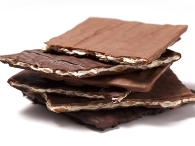 Sheets of matzoh cracker are enrobed in chocolate, broken into pieces and stacked together.