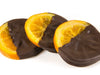 Slices of candied, glace orange, enrobed in 72% dark dairy-free chocolate are stacked together.