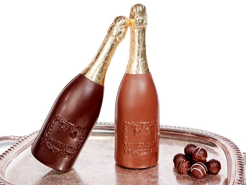 A milk and a dark chocolate Champagne bottle sit together on a silver platter. They have gold foiled tops and look like real-life champagne bottles.