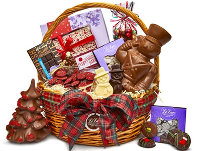A very large wicker basket is overflowing with chocolates and treats. The basket is tied with a holiday themed plaid ribbon.