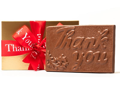 A large chocolate bar has Thank You and som efiligree embossedon the top. It comes in a gold box with a red ribbon with Thank You printed on it.