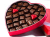 Thirty-five assorted chocolates sit inside a heart shaped box. The square, outer box stands nearby.